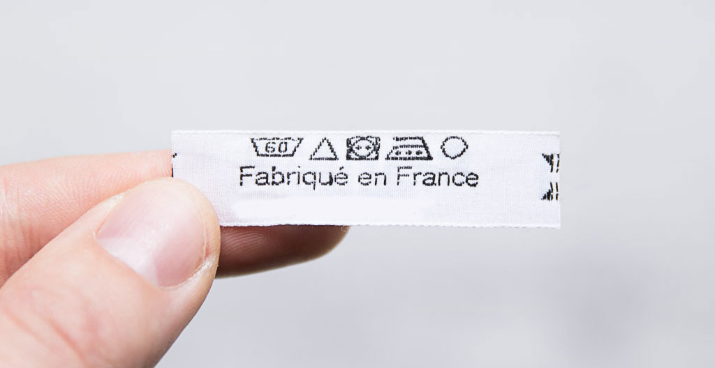 Main tenant l'étiquette d'entretien d'un gilet en maille avec symboles ISO 3758 de lavage visibles